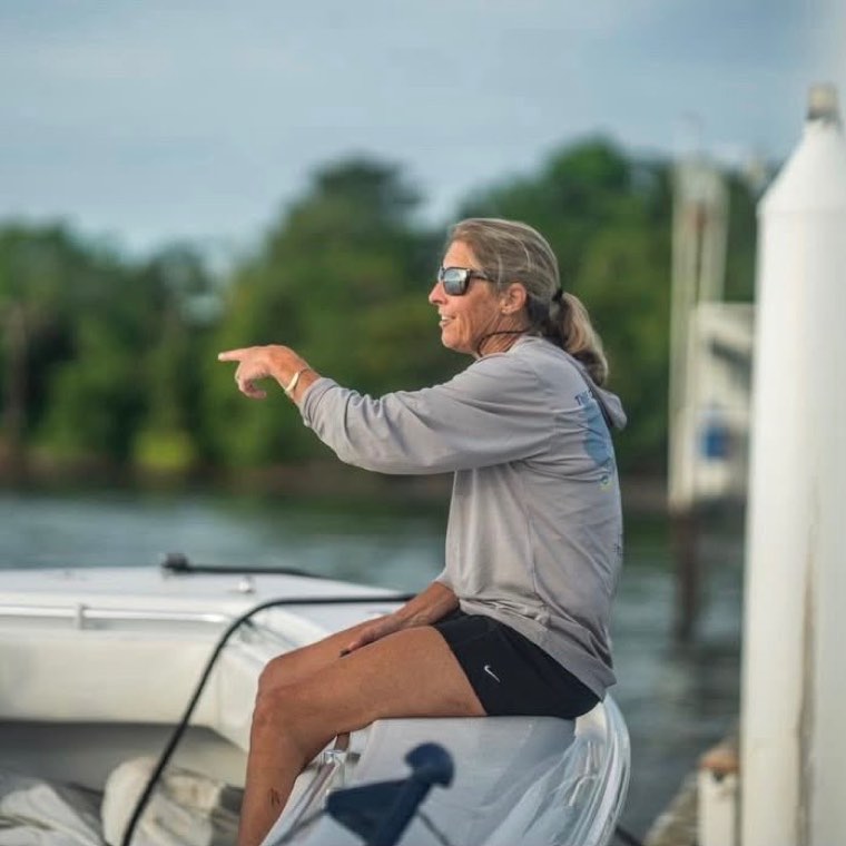 Cecile Shaw sitting on the bow of a boat at a dock, pointing out across the water.