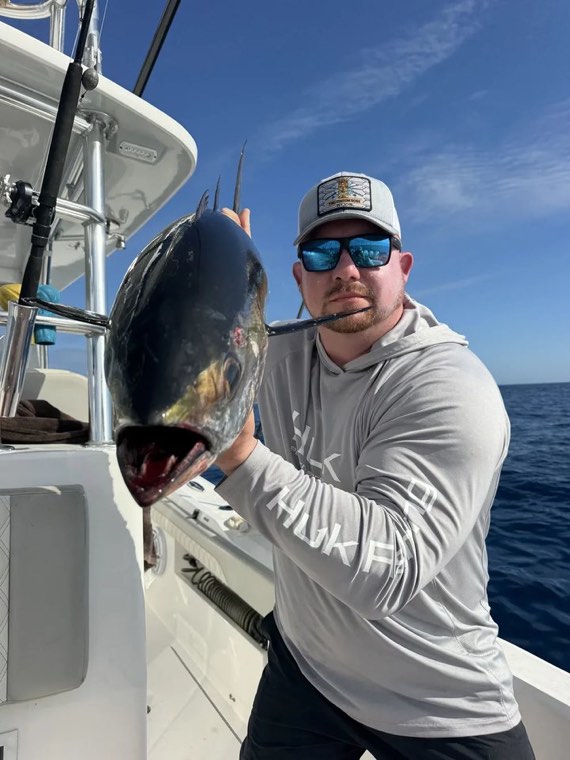 Jack Maglione on a boat deck offshore, holding a tuna he has just landed.
