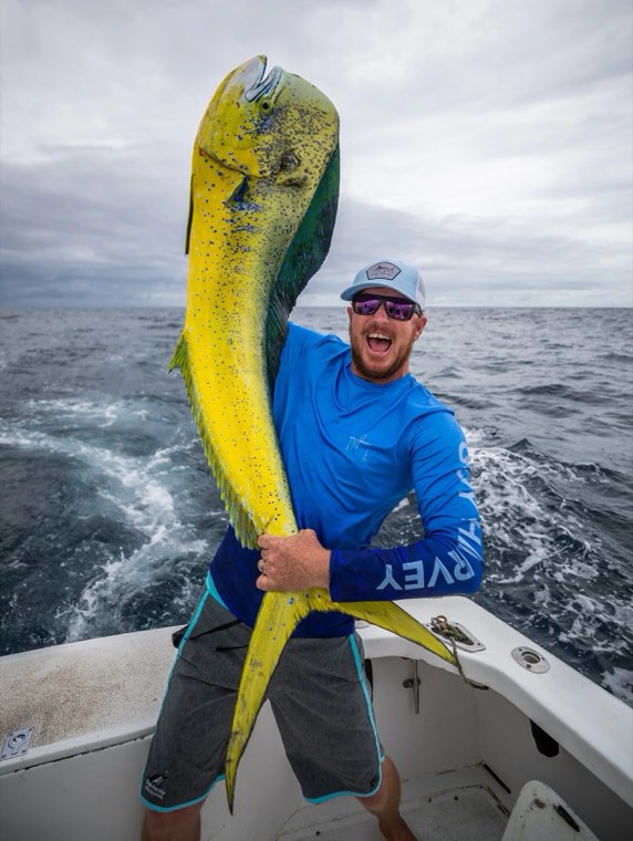 Captain Richie White holding a dorado aboard a boat under an overcast sky.