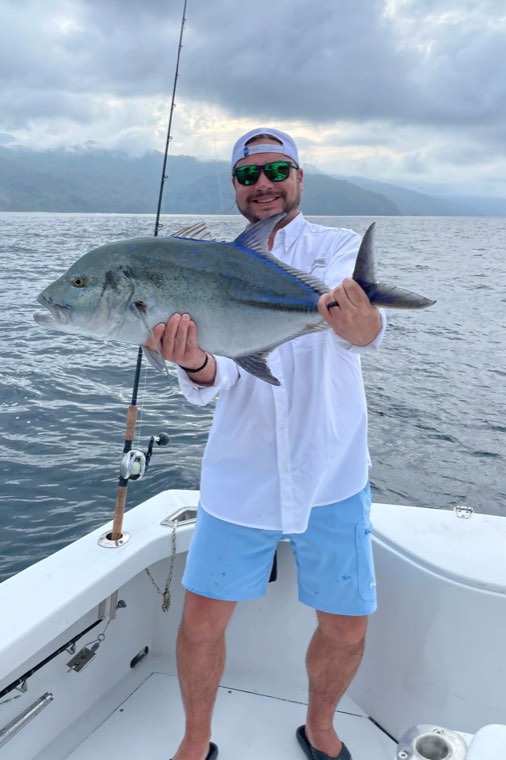 Sam Franzosa on a boat deck offshore, holding a jack he has just landed.