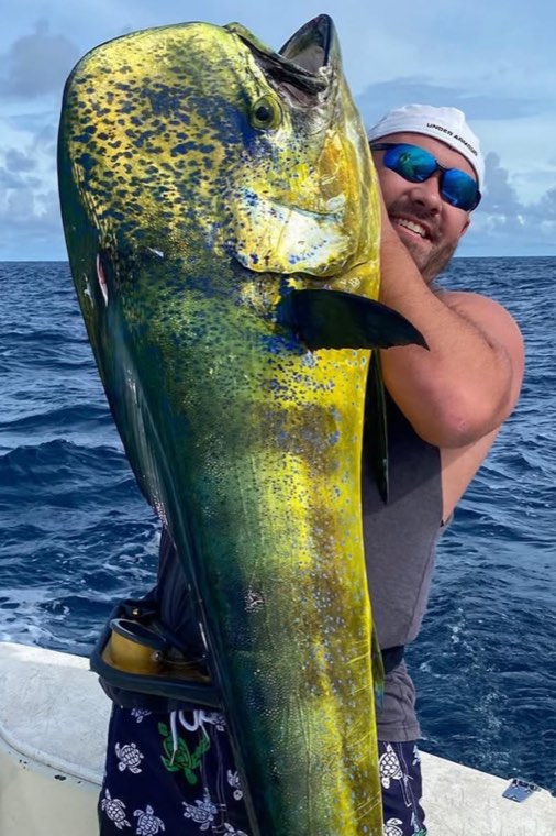 Sean Williams holding a large mahi-mahi aboard a boat in open water.
